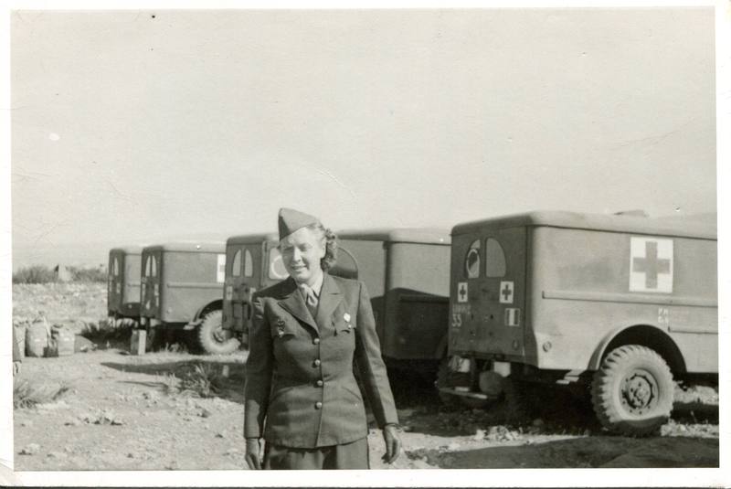 Crapette en uniforme et calot, debout devant une file d'ambulances neuves marquées d'une croix rouge.