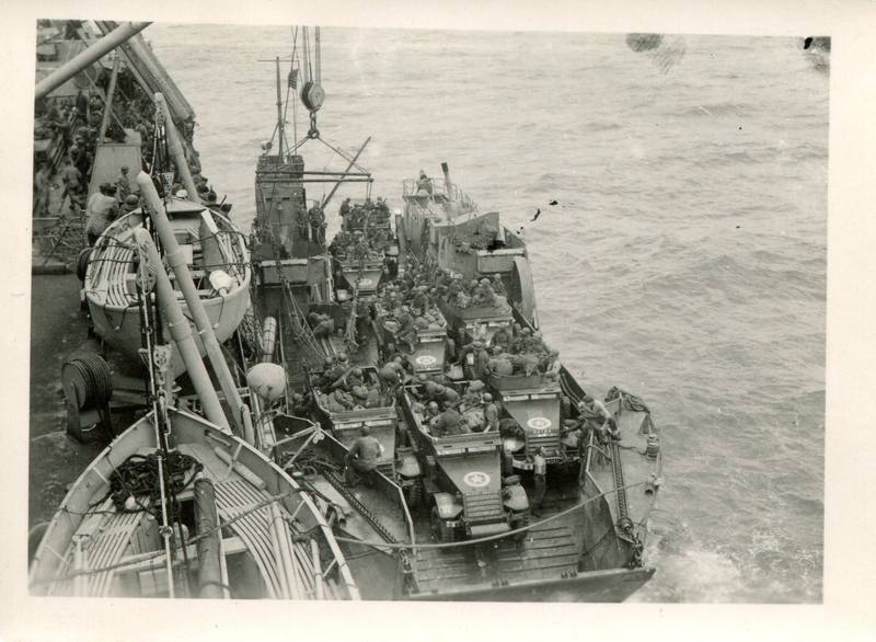 Depuis le pont d'un grand navire, vue sur une barge chargée de véhicules militaires, en pleine mer.